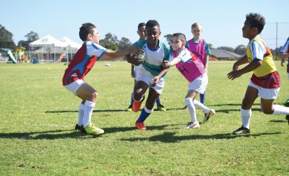 Young boys on a field playing rugby league, with a player being tackled